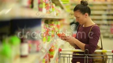 年轻女子从超市货架上挑选果汁。 她的超市里有很多东西.